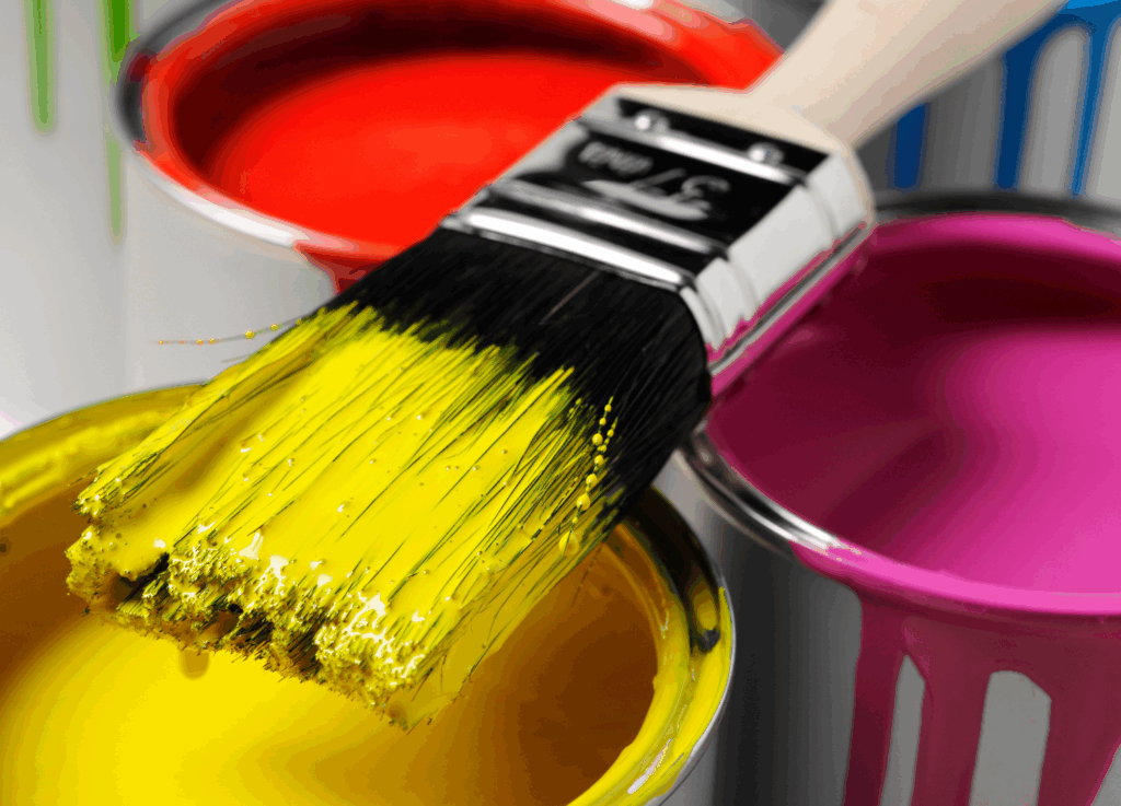 
Uma visão em close-up de um pincel de pintura com cerdas amarelas, gotejando sobre uma lata de tinta amarela. Ao fundo, latas de tinta nas cores magenta e vermelho parcialmente visíveis.